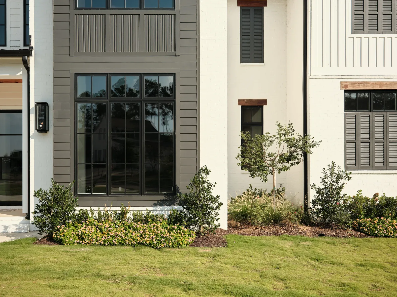 White home exterior with black framed windows, a trimmed lawn and planted beds
